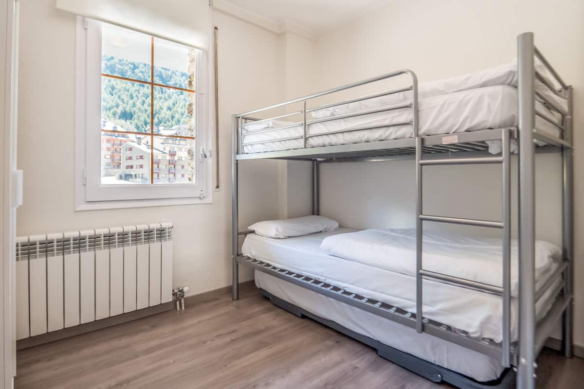 A bunk bed room with a window, radiator, and wooden flooring.