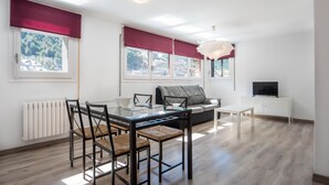 Una sala de estar moderna con una mesa de comedor de cristal, sillas negras, un sofá y un televisor sobre un mueble blanco.
