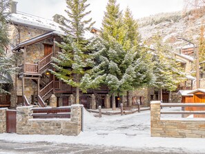 Un edificio de piedra con balcones de madera y un árbol cubierto de nieve al frente.