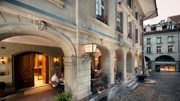 A historic hotel with a grand entrance, outdoor seating, and cobblestone streets. - Hotel Stadthaus (Burgdorf)