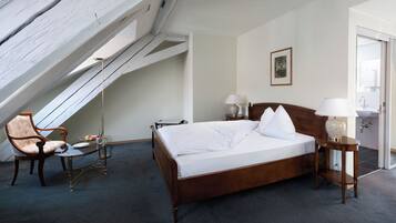 Une chambre d’hôtel avec un lit en bois, une chaise, une petite table et une lampe.