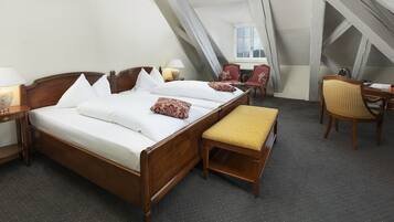 A bedroom with a wooden bed, a bench, two chairs, a desk, and a window.