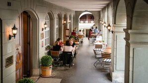 A corridor with tables and chairs, potted plants, and a balcony in the background. - Hotel Stadthaus (Burgdorf)
