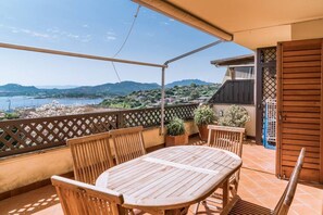 Ein Holztisch mit Stühlen auf einem Balkon, mit Blick auf das Meer und die Hügel.