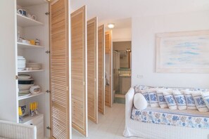 Une pièce avec un canapé, une armoire en bois et, au fond, une salle de bain.
