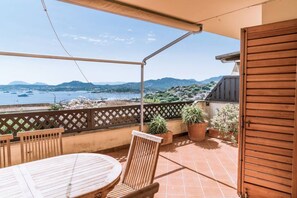 Eine Terrasse mit Tisch und Stühlen, Blumentöpfen und Blick auf das Meer und die Hügel.