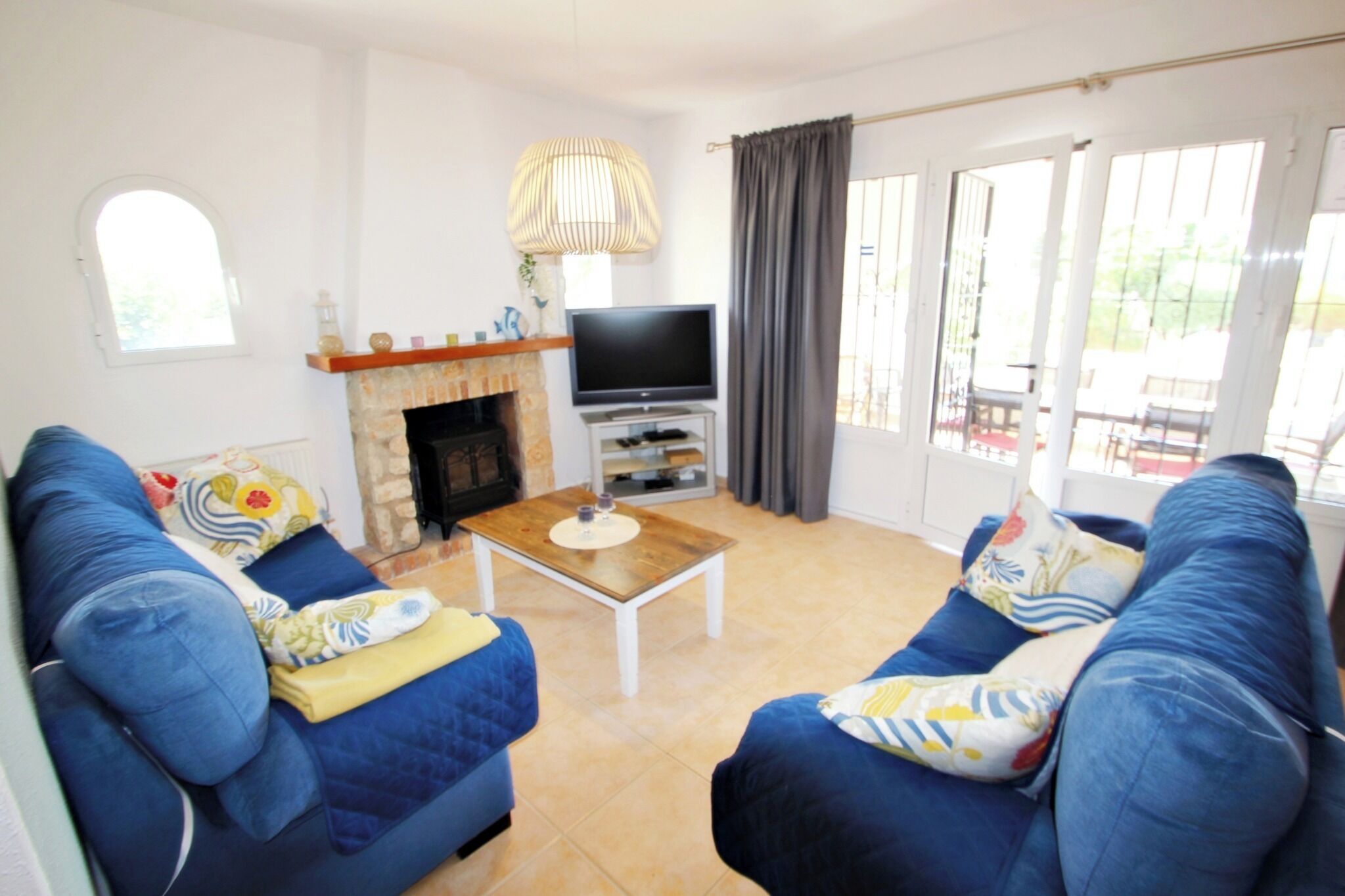 A living room with two blue sofas, a TV on a stand, a fireplace, and a large window with curtains.