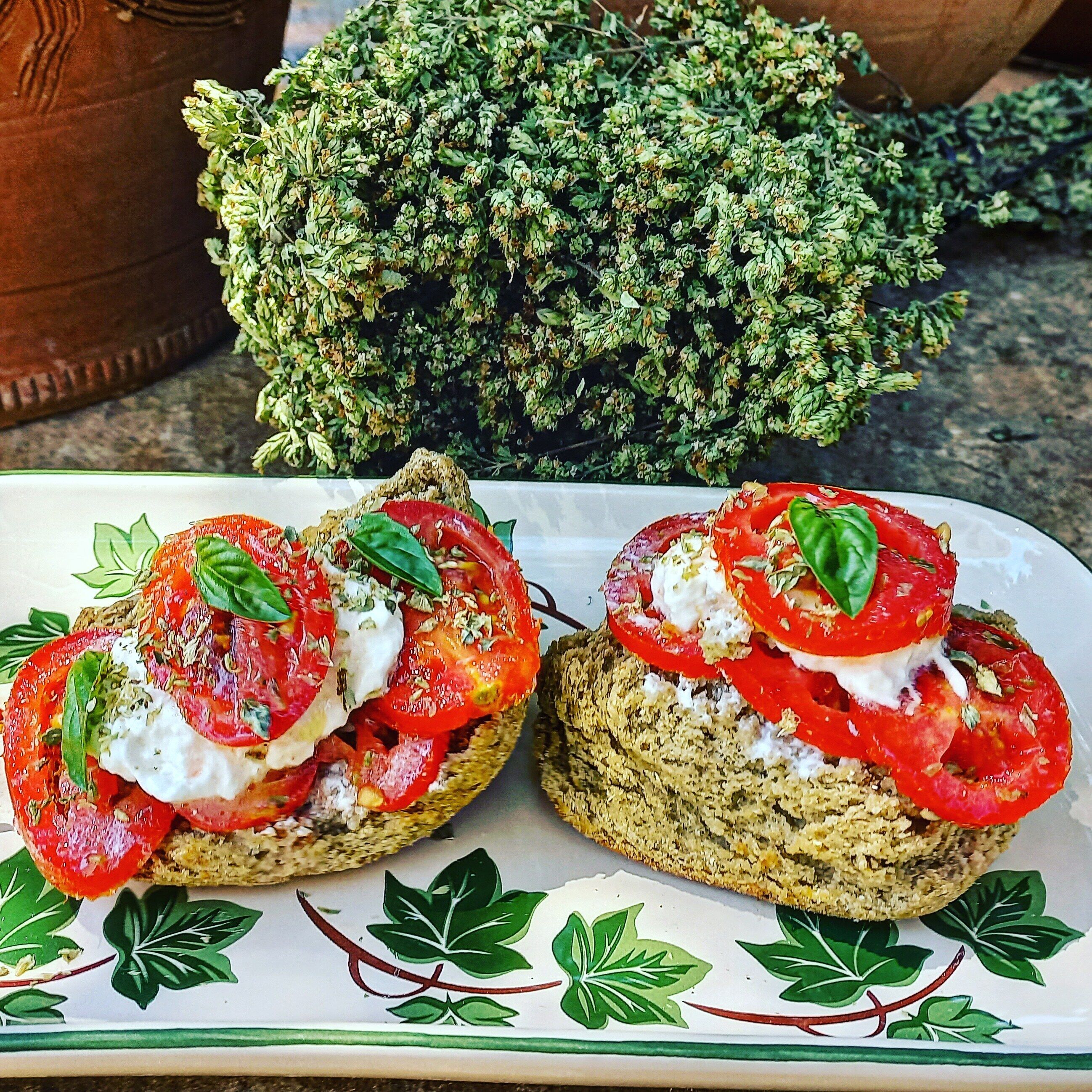 Dos sándwiches abiertos con tomate y cobertura cremosa, servidos en un plato con un diseño de hojas decorativas.