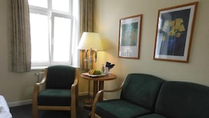 Ein Hotelzimmer mit einem grünen Sofa, einem Holzsesseln, einem kleinen runden Tisch mit einer Lampe und zwei gerahmten Bildern an der Wand.