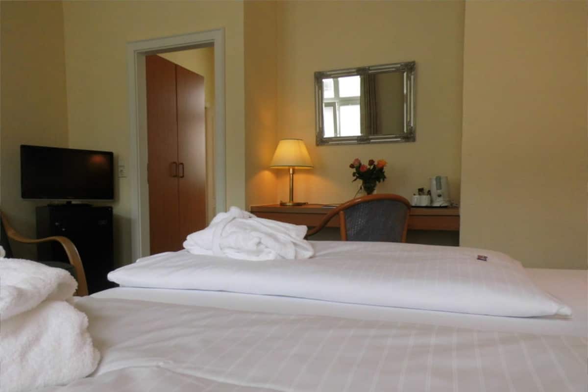 Une chambre d’hôtel avec un lit, un bureau avec une lampe, une télévision et un miroir au mur.