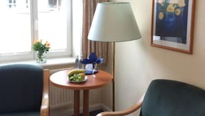 Ein Hotelzimmer mit zwei grünen Sesseln, einem kleinen runden Tisch mit Lampe, einer Blumenvase und einem gerahmten Bild an der Wand.