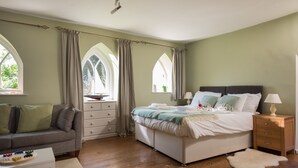 Um quarto com cama, mesa de cabeceira, cômoda, sofá e janela com cortinas.