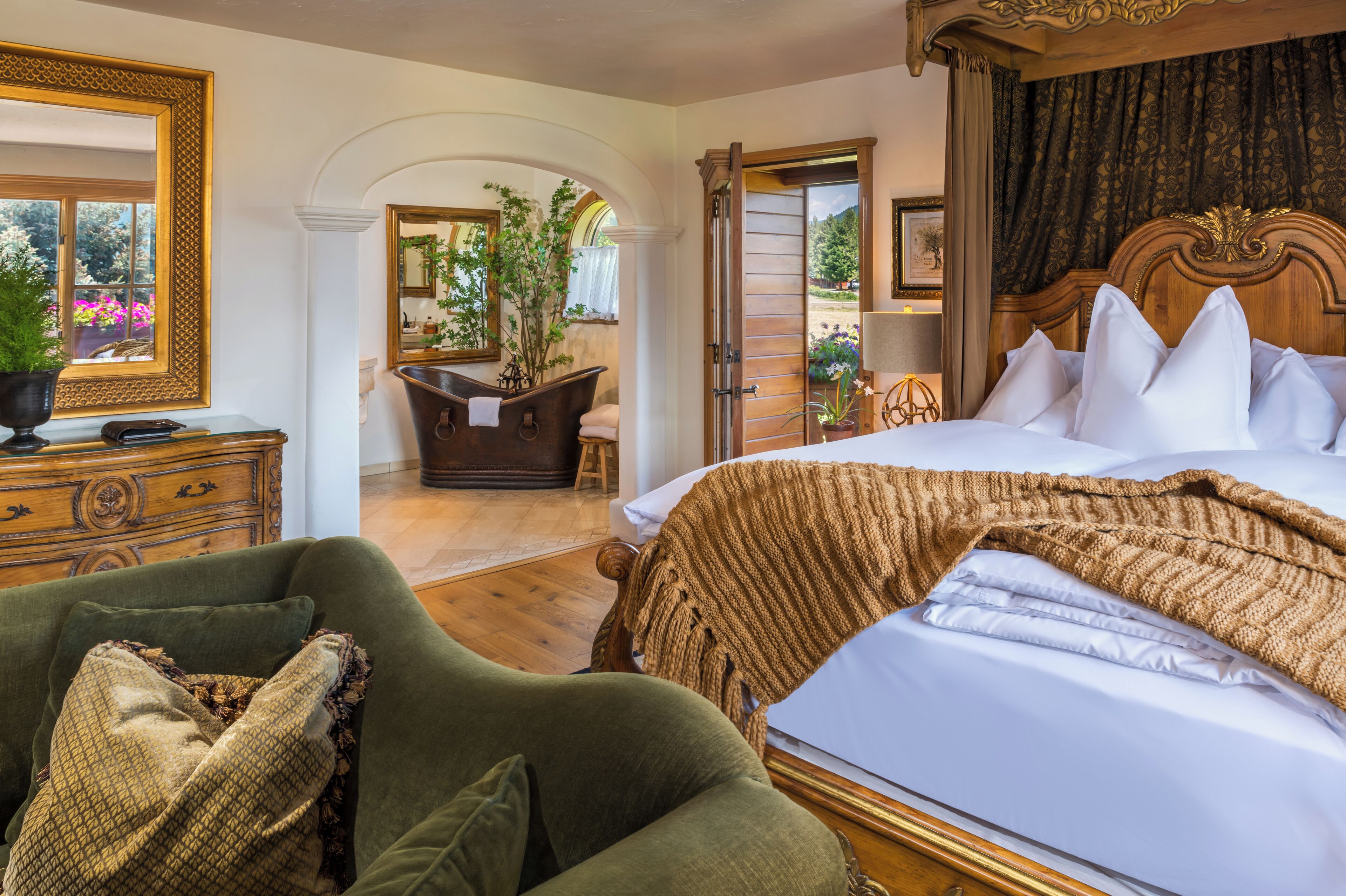 A bedroom with a large bed, a wooden headboard, a green armchair, a dresser, and a mirror.