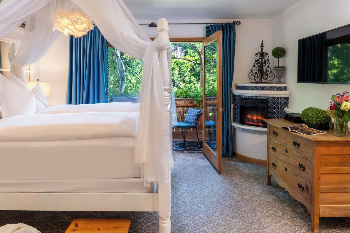 Une chambre à coucher avec un lit à baldaquin, une cheminée, une télévision et une vue sur l’extérieur.