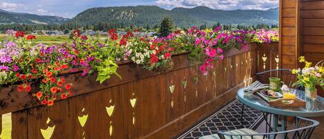 Een houten balkon met uitzicht op bergen, een tafel met stoelen en diverse bloemen.