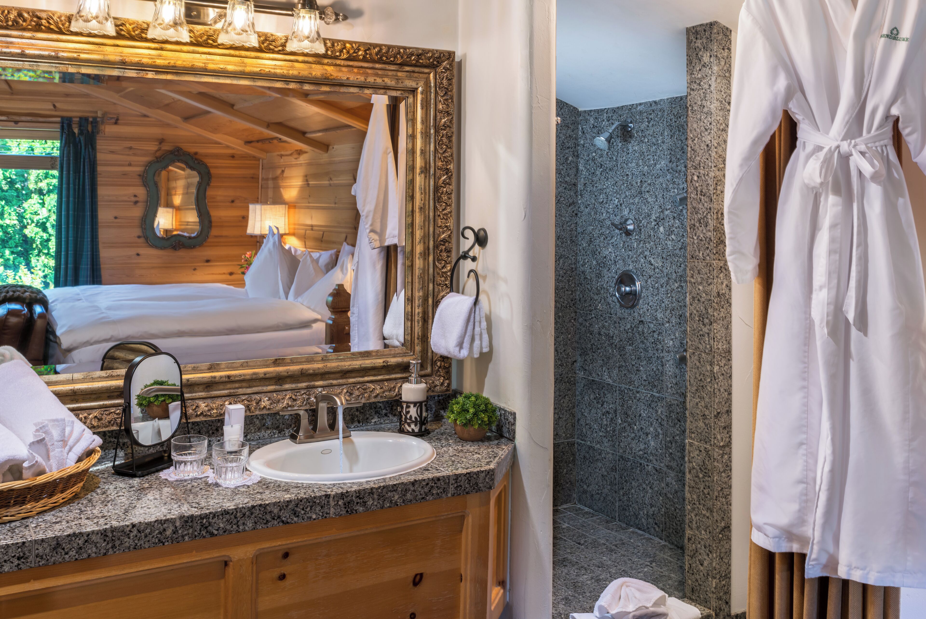 A bathroom with a large mirror, a sink, a shower, and a robe hanging on the wall.