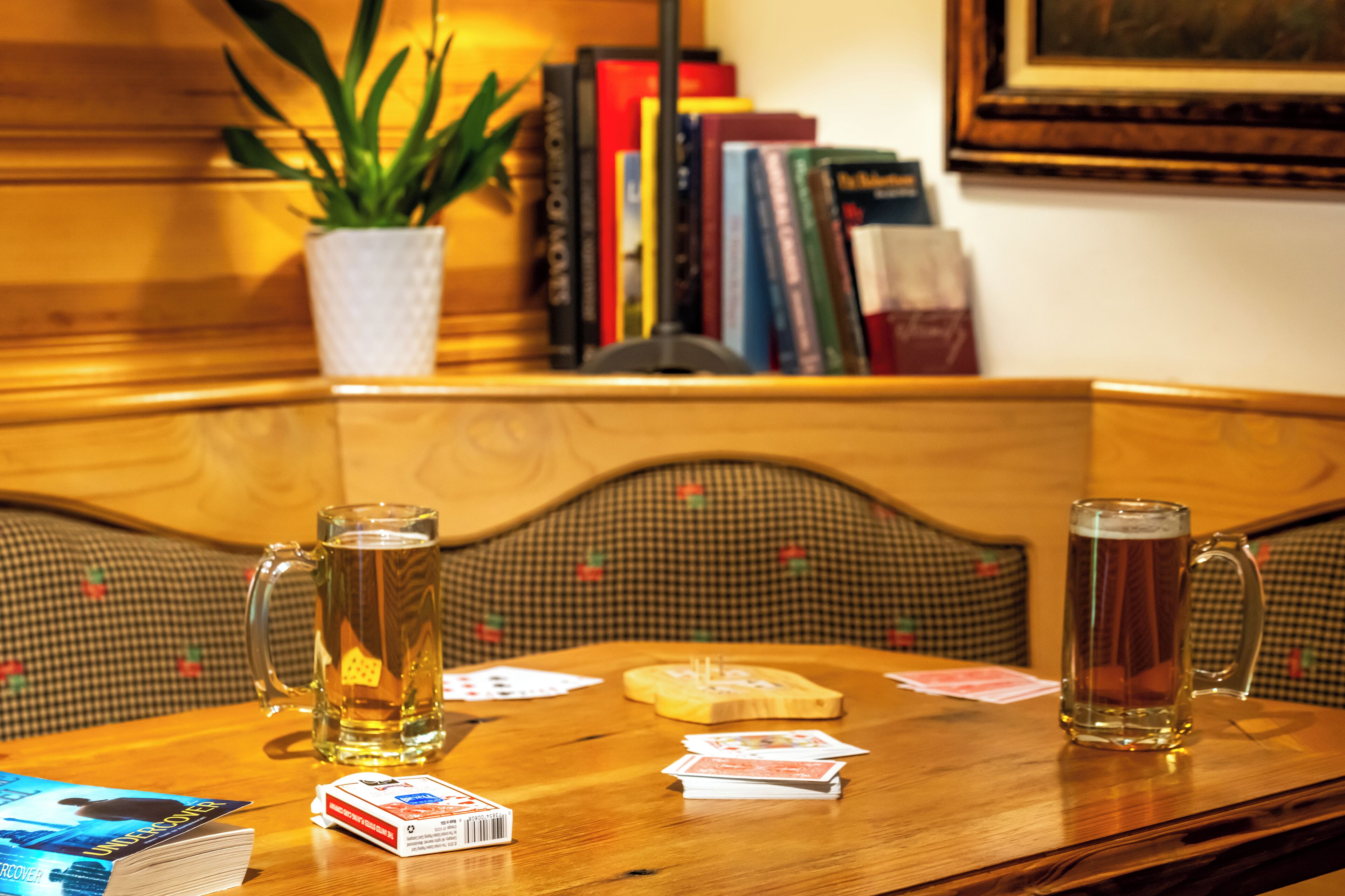 Ein Holztisch mit zwei Bierkrügen, Spielkarten und einem Buch.