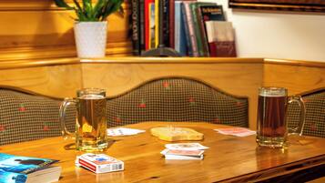 Ein Holztisch mit zwei Bierkrügen, Spielkarten und einem Buch.