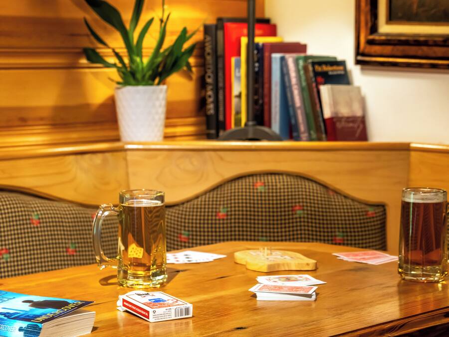 Ein Holztisch mit zwei Bierkrügen, Spielkarten und einem Buch.
