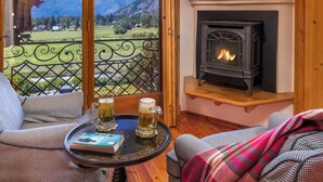 A cozy room with a fireplace, a balcony with a view of mountains, and two chairs with a table in the foreground. - Abendblume - Adults Only (Leavenworth)