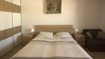 A bedroom with a large bed, two bedside tables with lamps, a brown sofa, and a painting on the wall.