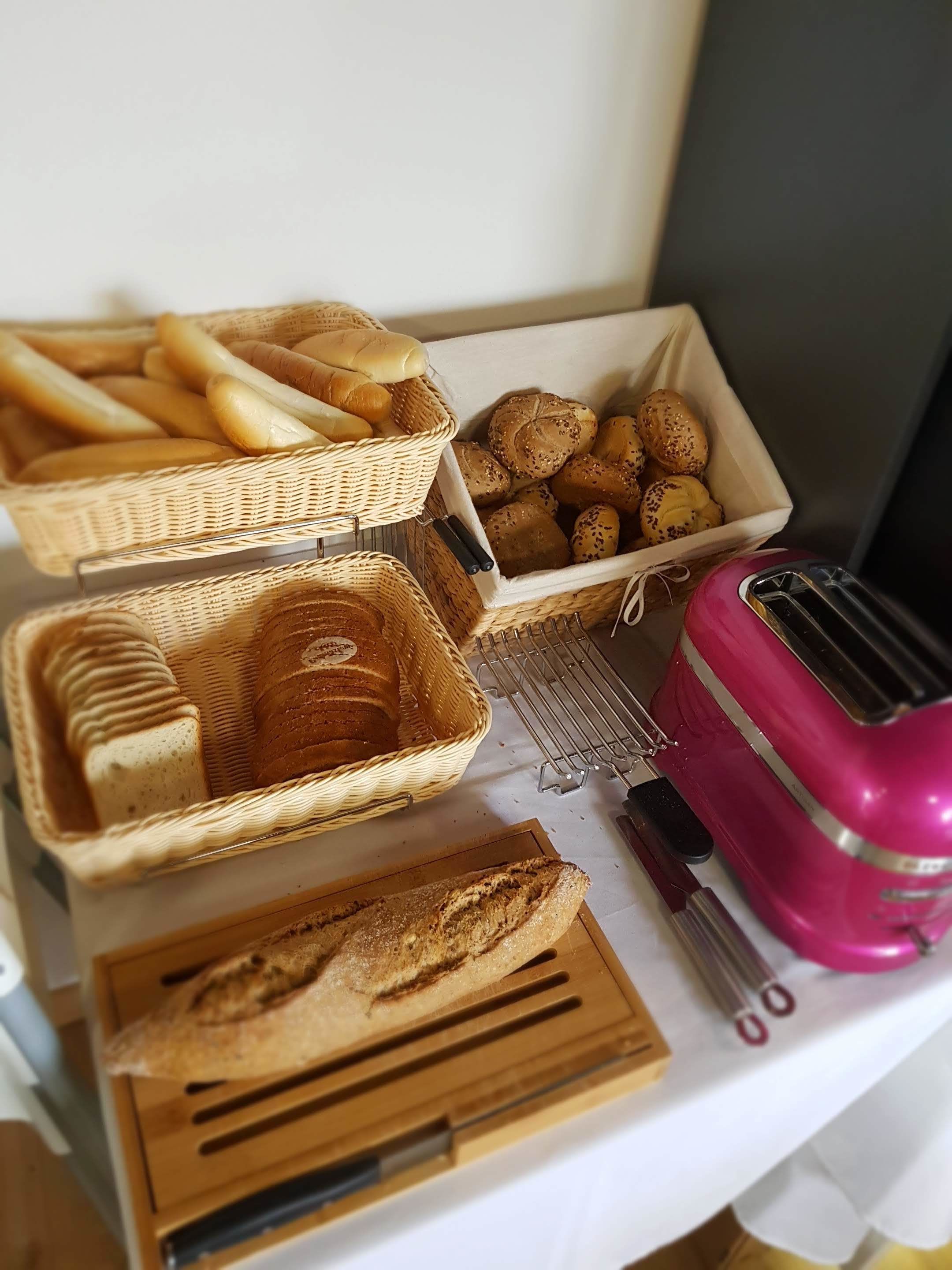 A kitchen counter with various bread items in wicker baskets and a pink toaster.