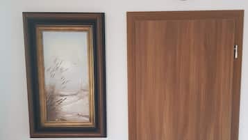 A room with a wooden door, a framed picture on the wall, and a clock.