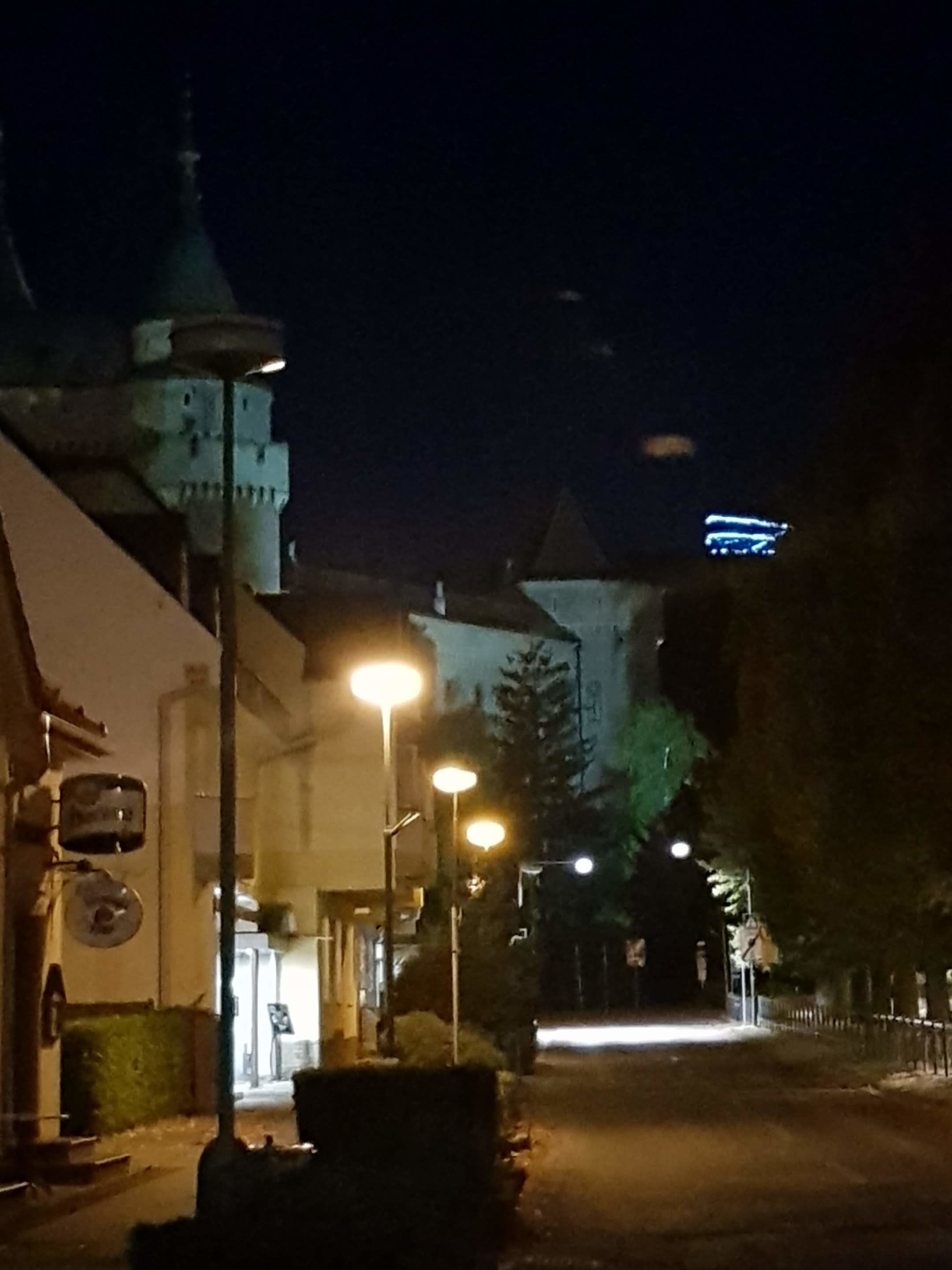 A nighttime street view with a tower in the background, street lamps, and buildings along the road.