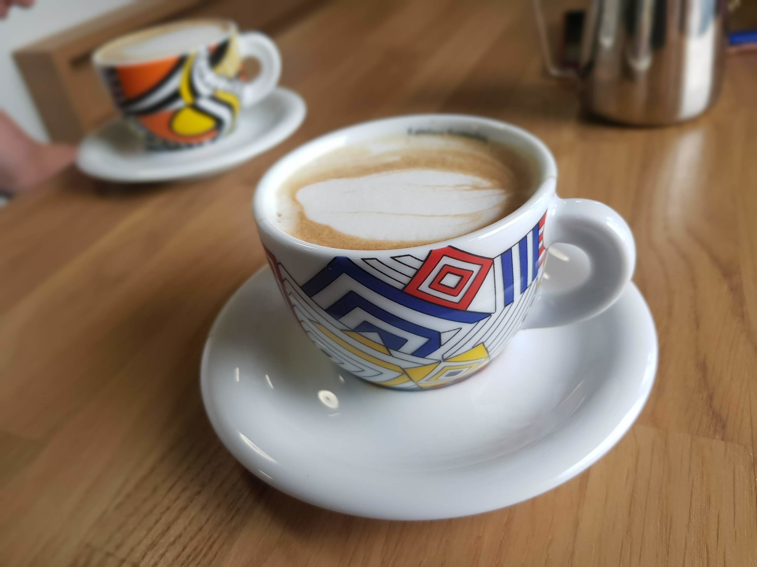 A cup of coffee on a saucer with a colorful geometric pattern.