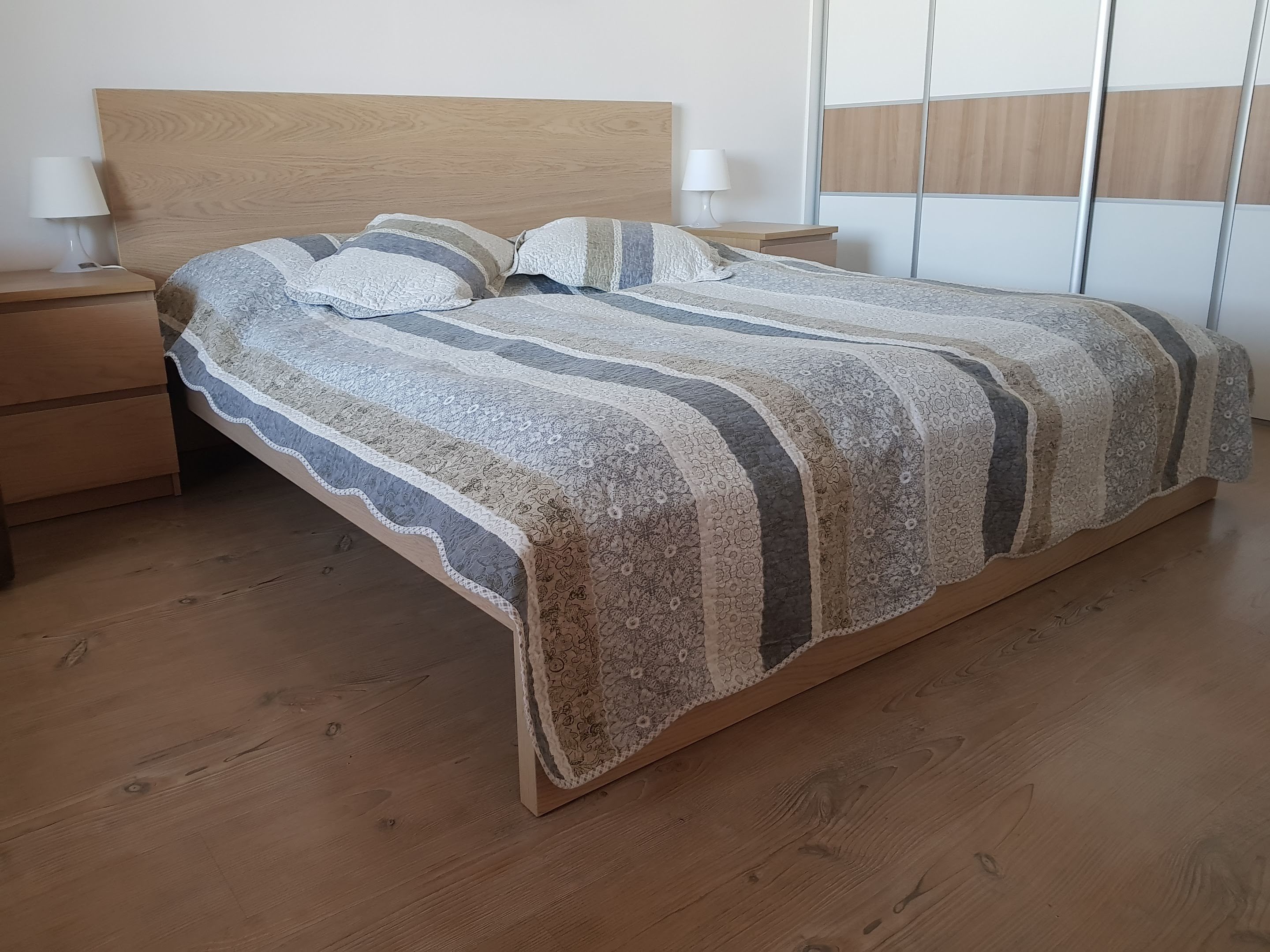 A bedroom with a wooden bed, two bedside tables with lamps, and a wooden floor.