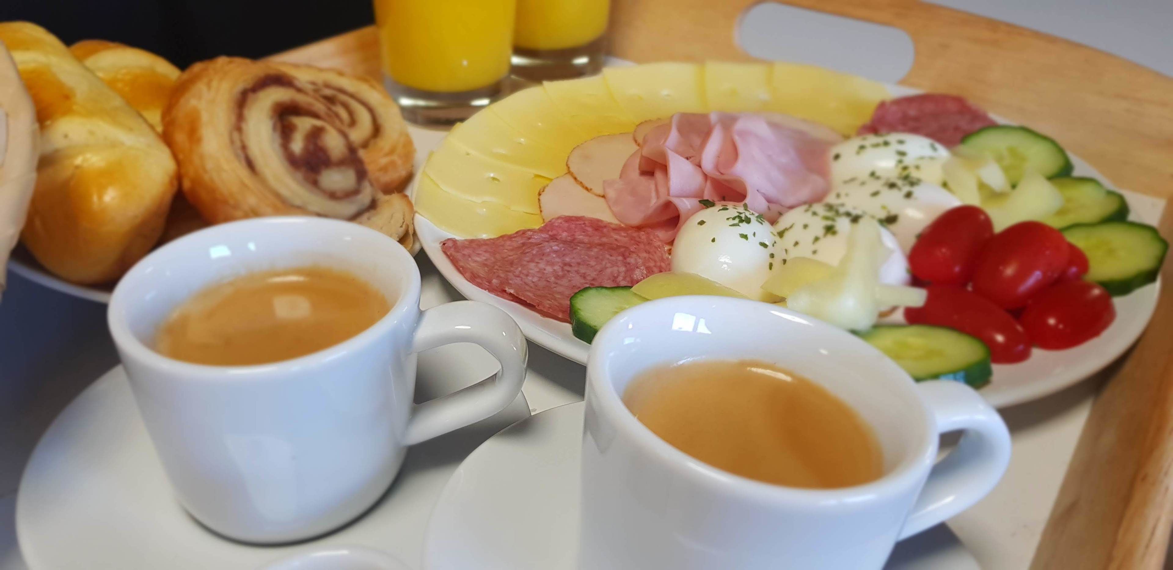 Een ontbijfwagen met croissantjes, ham, kaas, tomaten, komkommers en een glas sinaasappelsap.