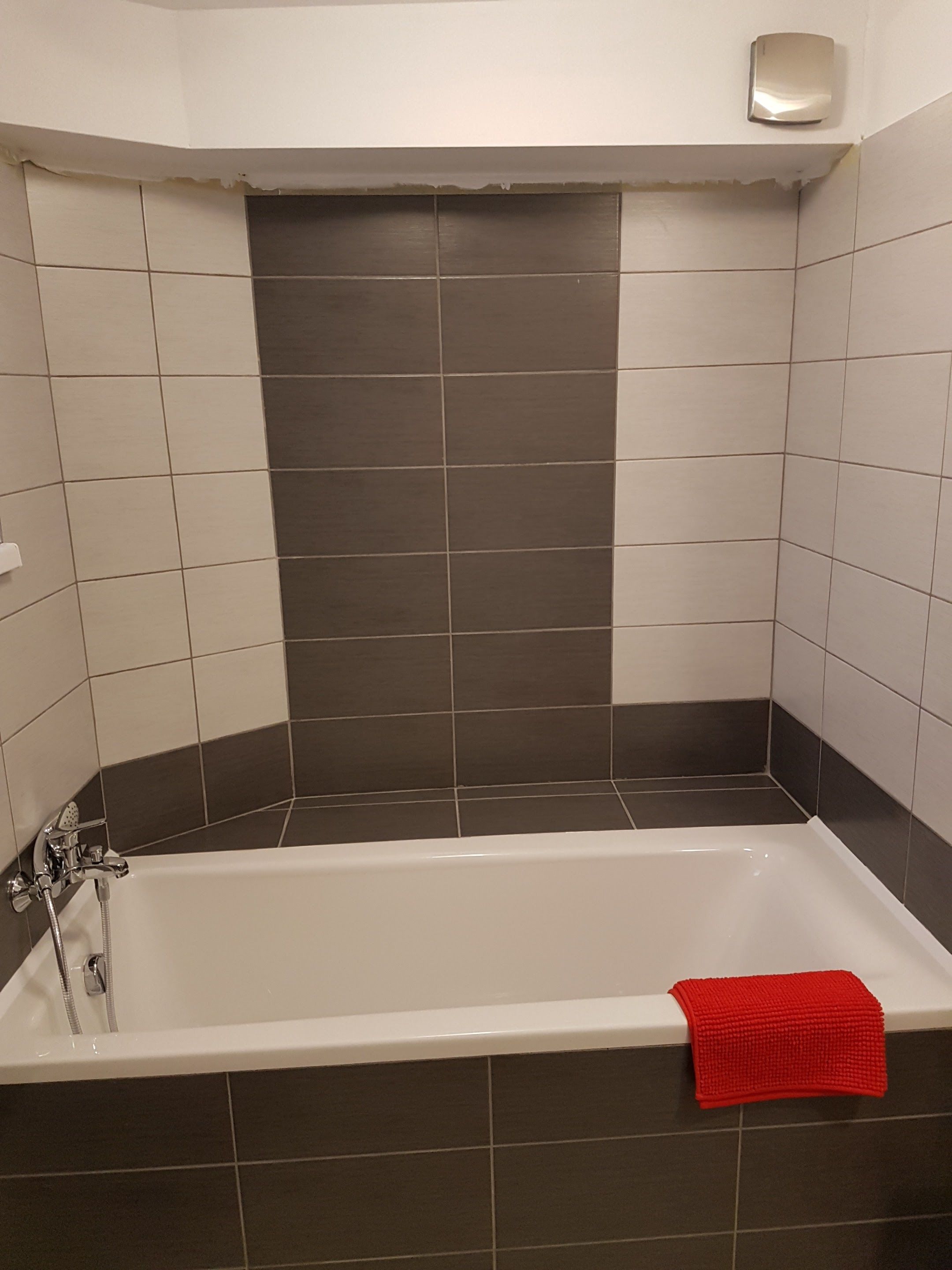 Un baño con bañera, paredes con azulejos en tonos oscuros y claros, una toalla roja y un secamanos.