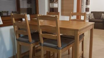 A dining area with a wooden table and chairs, a window with blinds, and a door with a decorative curtain.
