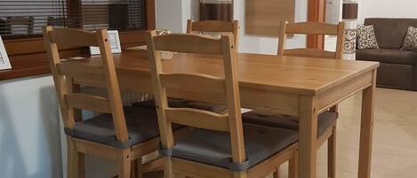 Un coin repas avec une table et des chaises en bois, une fenêtre avec des stores et une porte agrémentée d’un rideau décoratif.