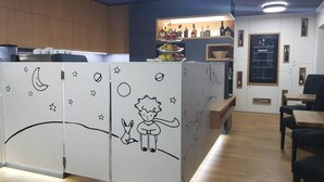 Una zona de bar con mostrador de madera, estanterías con botellas y un área de asientos con mesa y sillas.