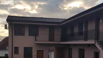 Um edifício com telhado em cerâmica, varanda com grades de metal e pátio pavimentado.