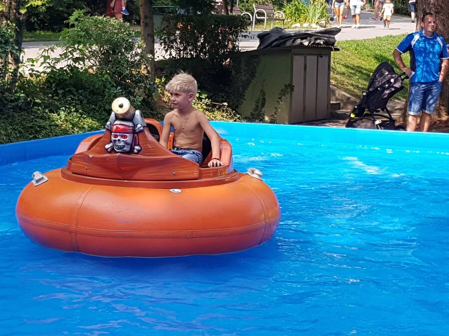 Niño en un bote inflable naranja con decoración de calavera en una piscina.