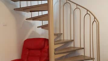 Un escalier en colimaçon moderne, avec une finition beige, un fauteuil en cuir rouge doté d’un coussin et un plancher de couleur claire.