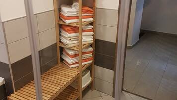A bathroom with a wooden shelf holding folded towels, a wooden bench, and a white bathtub.