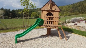 Un parque infantil con un tobogán de madera y una casita de juegos.