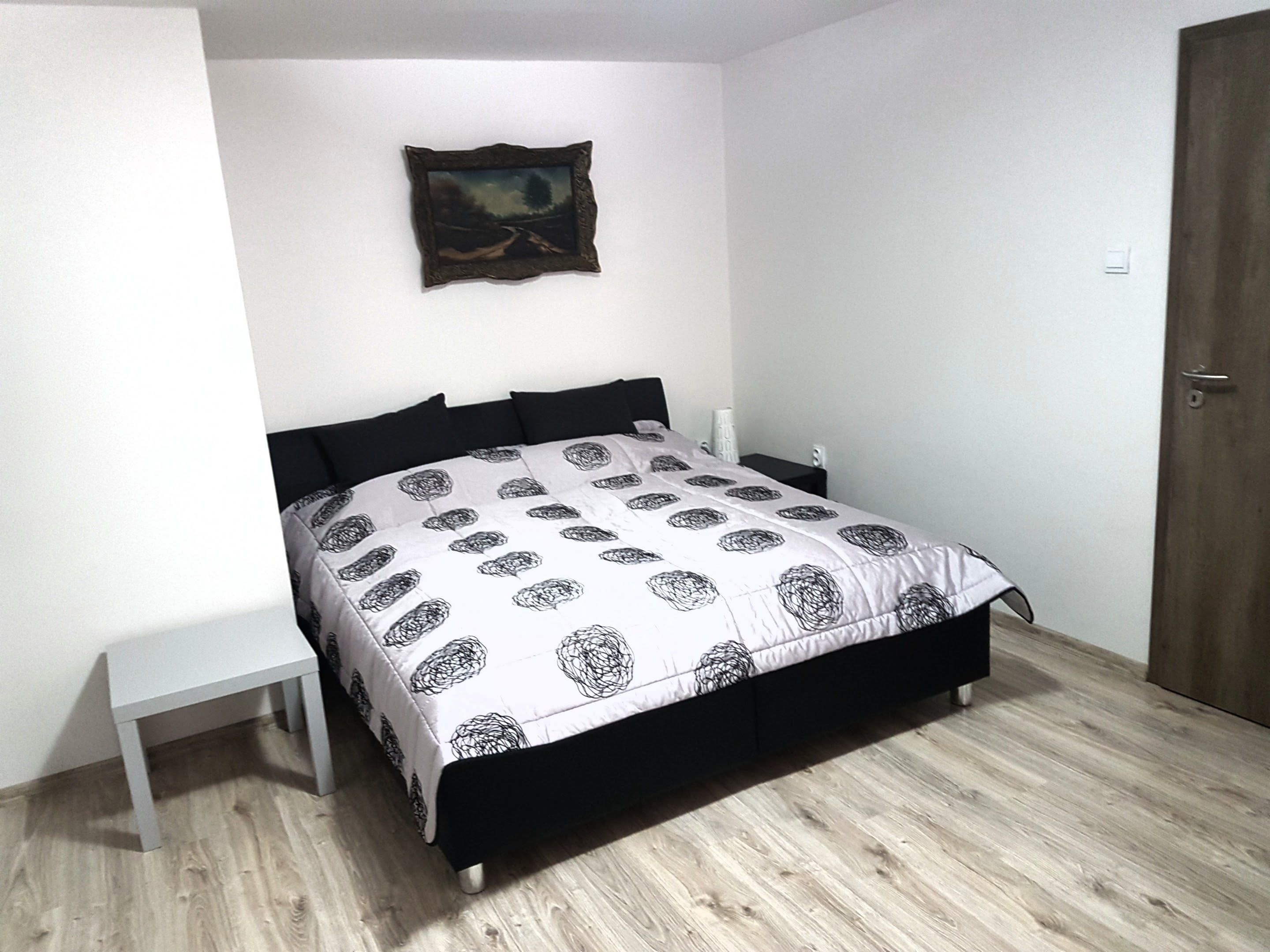 Une chambre à coucher avec un lit, une table de chevet, un tableau accroché au mur et une porte en bois.