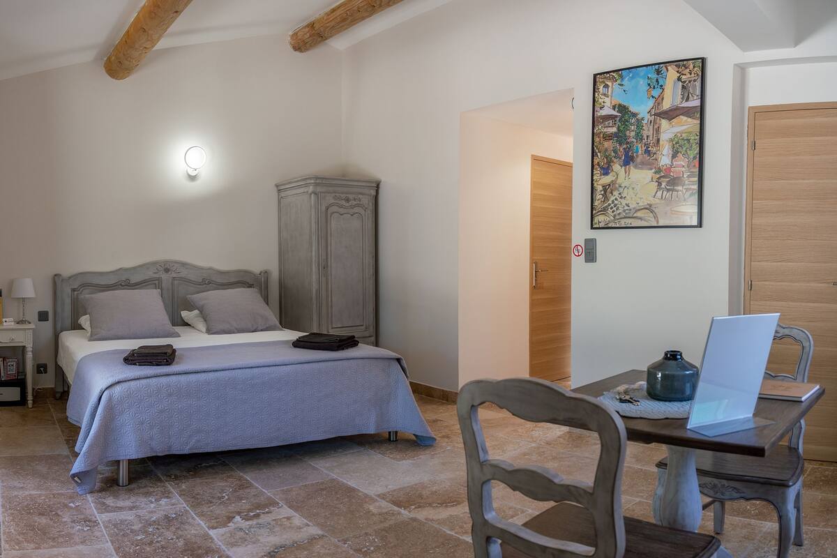 Quarto com cama, mesa de cabeceira, abajur e um quadro na parede.