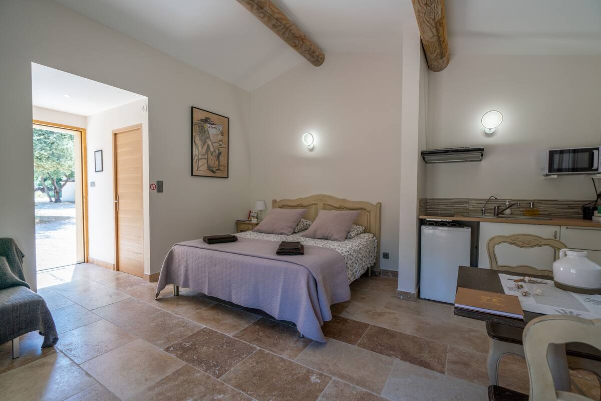 Quarto com cama, mesa de cabeceira e escrivaninha com cadeira. Uma porta dá acesso a uma varanda.