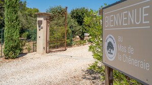 Un cartel de bienvenida en la entrada de Mas de la Chèneraïe, con una reja y un camino de grava.