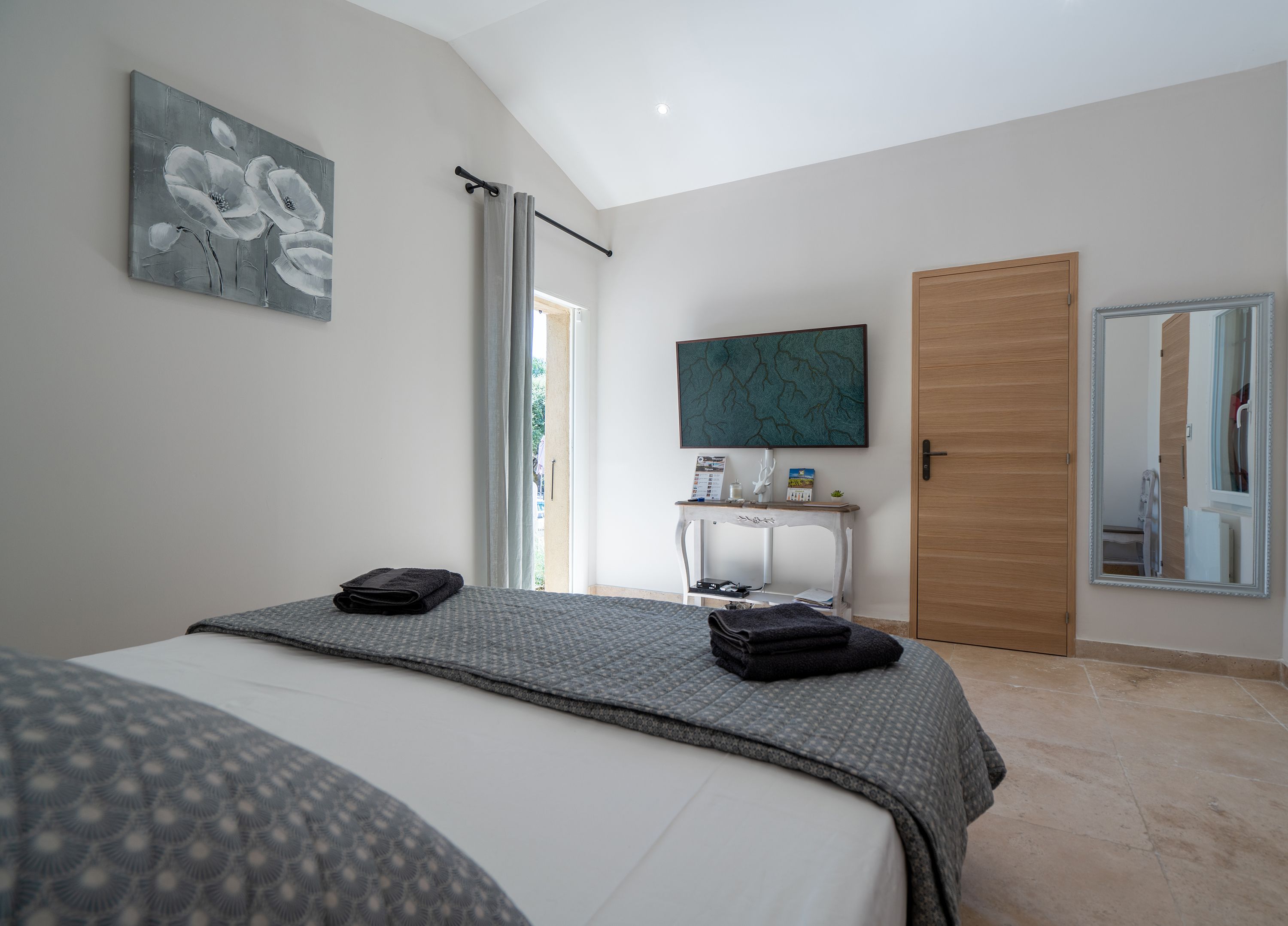 A bedroom with a bed, a bedside table, a mirror, and artwork on the walls.