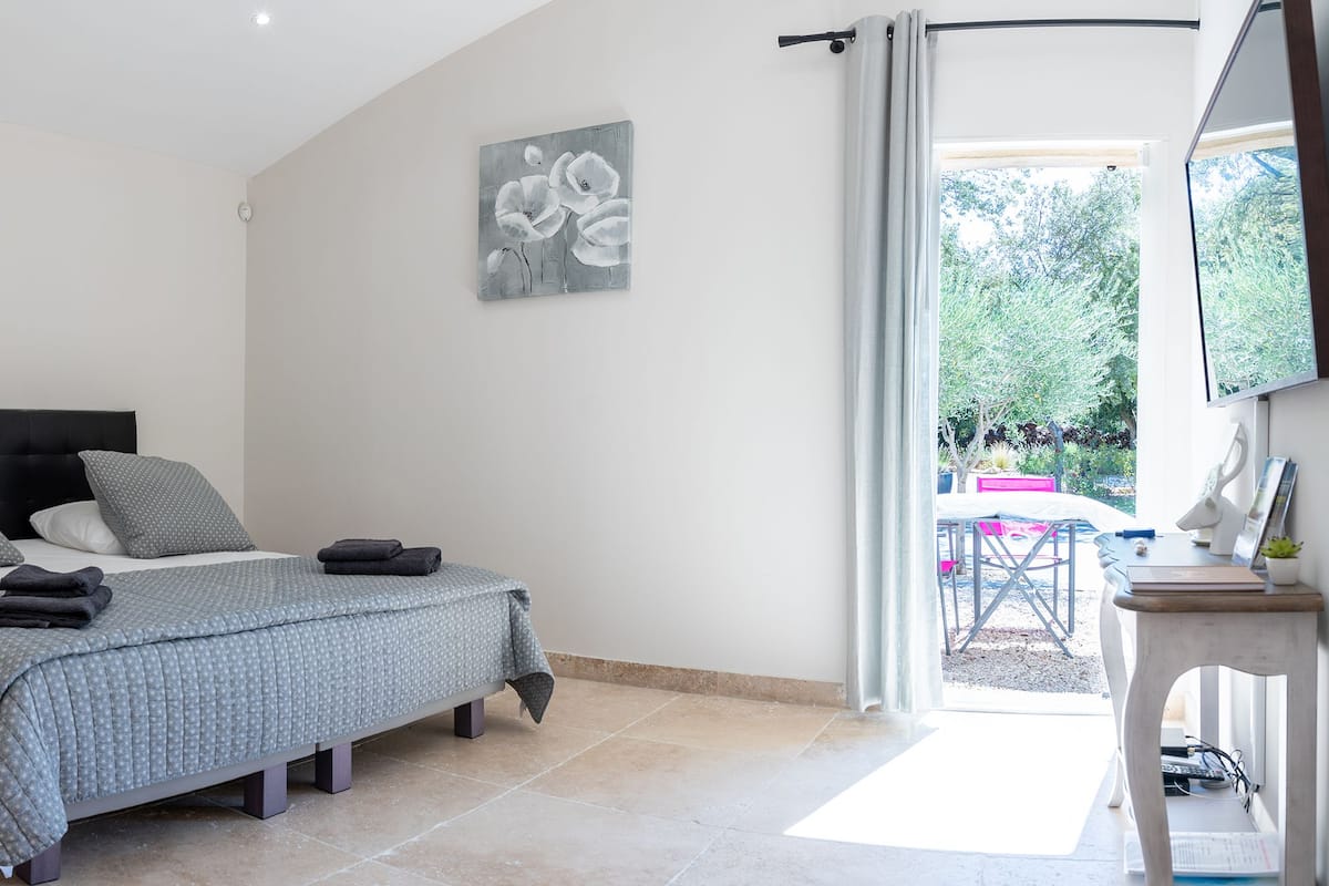 Quarto com cama, mesas de cabeceira, uma cadeira e uma escrivaninha com cadeira.