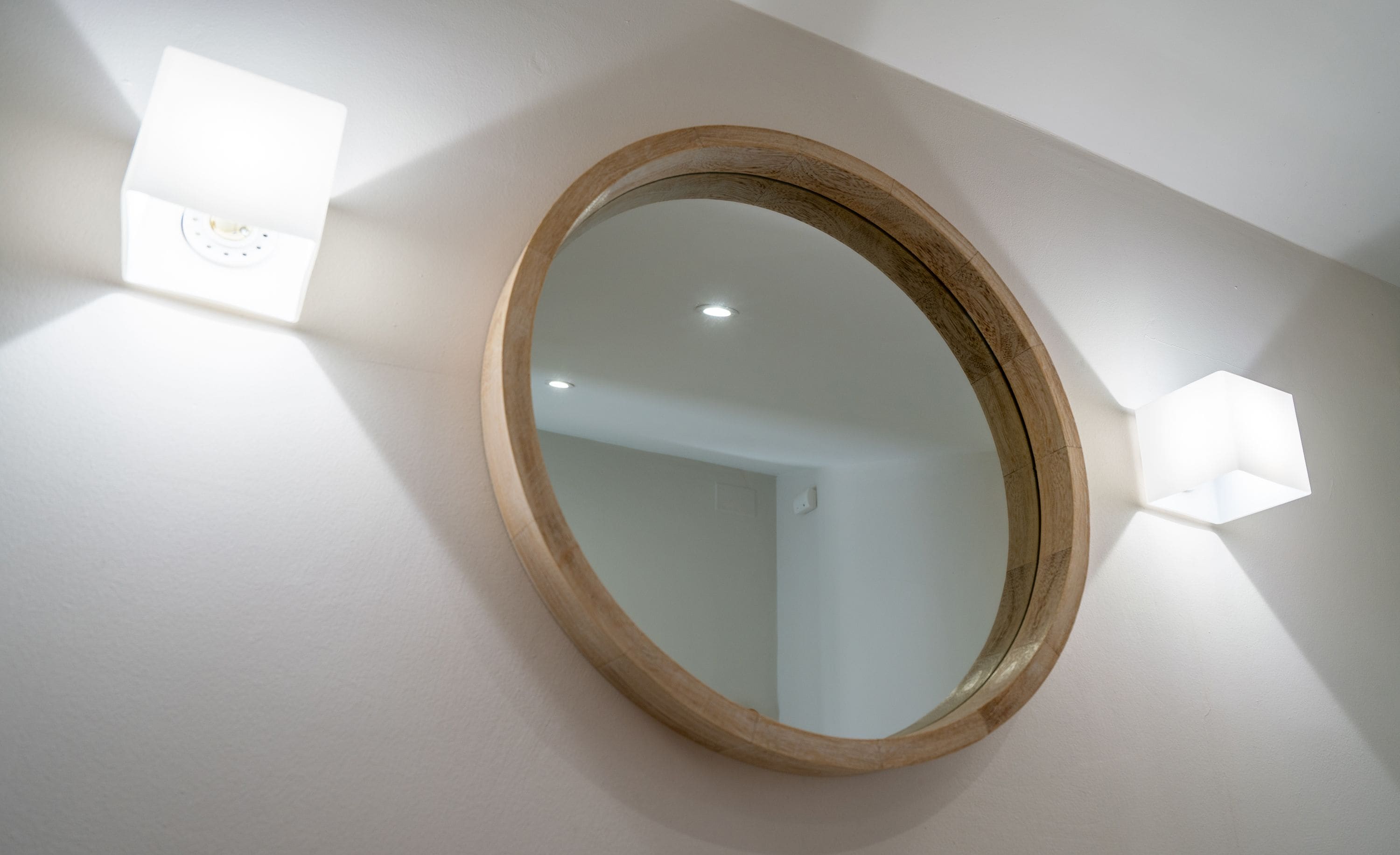 A round mirror with a wooden frame mounted on a white wall.