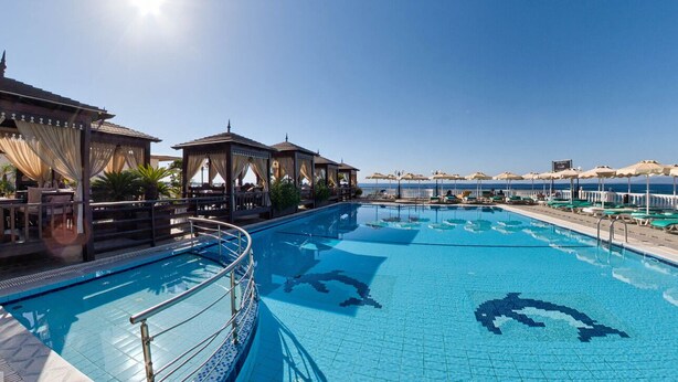 A swimming pool with clear blue tiles, surrounded by lounge areas and umbrellas. - Coralli Apartments (Rhodes)