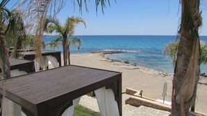 A beachside view with a wooden deck, white curtains, and palm trees. - Coralli Apartments (Rhodes)