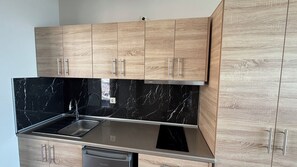 A modern kitchen with wooden cabinets, a black marble backsplash, and stainless steel appliances. - Coralli Apartments (Rhodes)